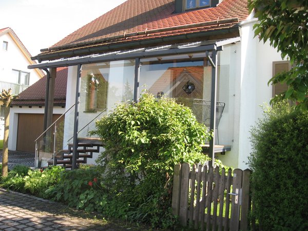 Hauseingansgüberdachung mit Stahltreppe verzinkt lackiert, Geländer aus Edelstahl und Glas, Belag                   aus Tropenholz